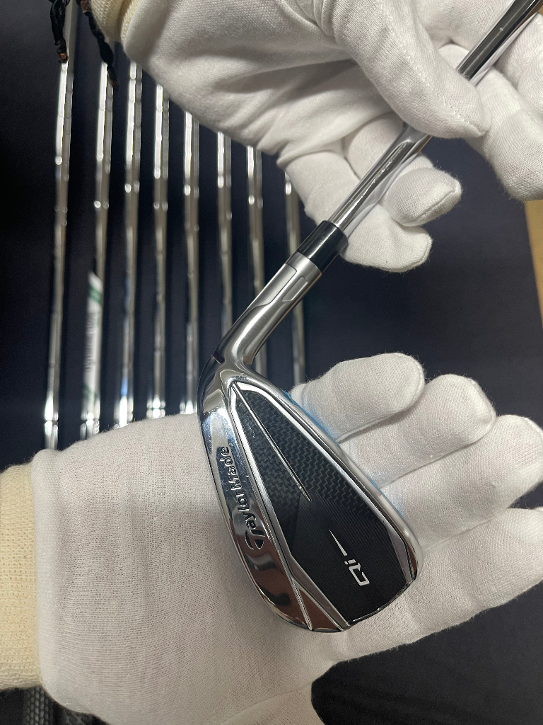White gloved hand holding a TaylorMade Qi iron during professional golf club detailing